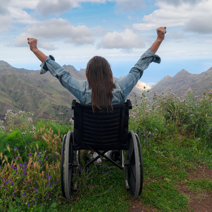 person in wheelchair raising arms in victory, viewed from behind