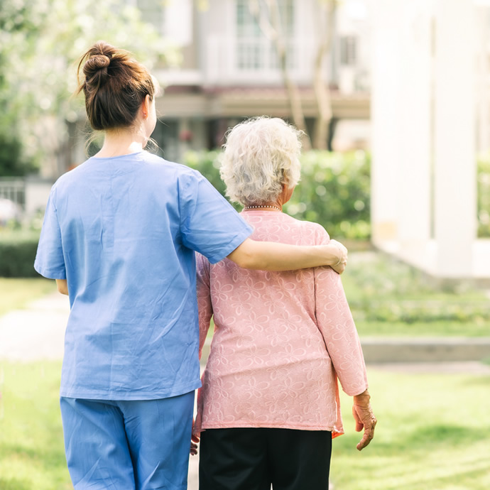 caregiver and senior walking outdoors, viewed from behind