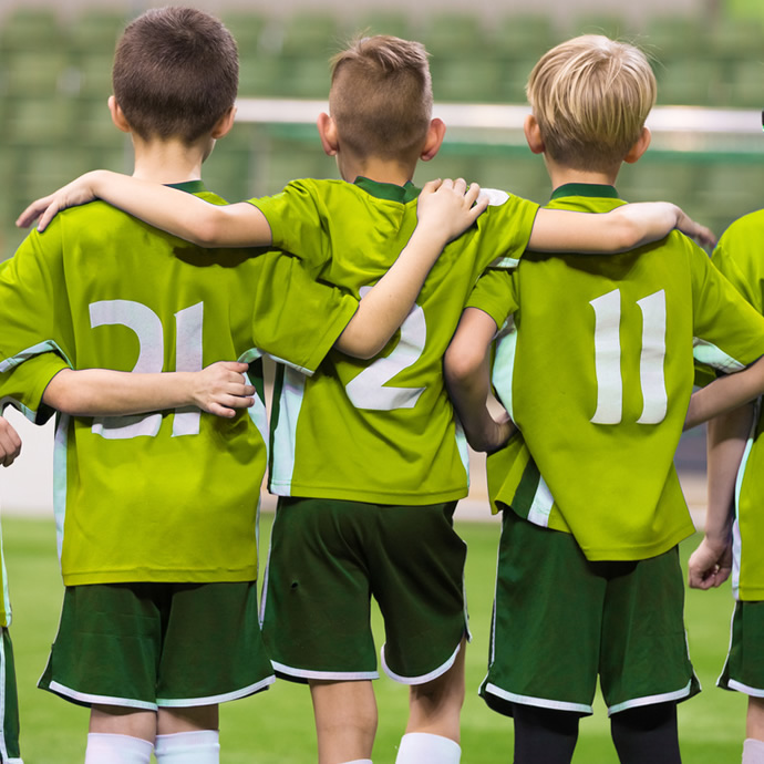 several pre-teen youth in sports uniforms with arms on each others' shoulders, viewed from behind